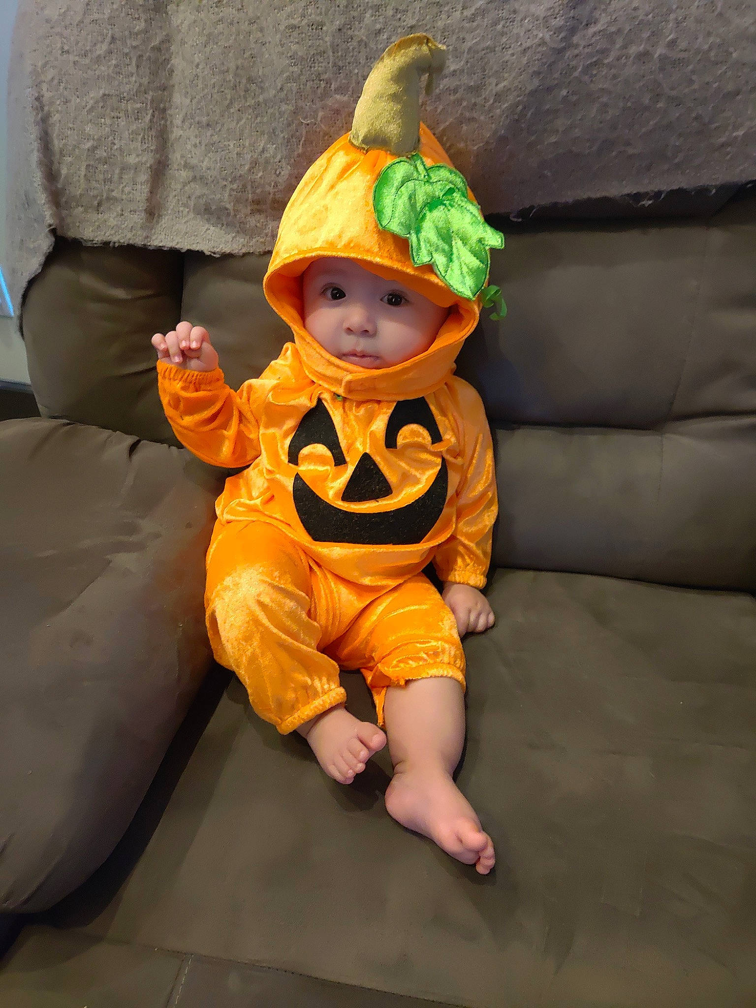 Angel is registered to the contest to win money with this photo: baby, baby_toddler_clothing, beanie, calabaza, comfort, costume, costume_hat, couch, eye, fictional_character, flooring, fun, headwear, person, personal_protective_equipment, play, pumpkin, room, sitting, sleeve
