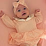 baby, infant, headband, peach, dress, frills, cute, lying_down, pink_background, smiling, arms_up, closeup, soft_texture, adorable, child, portrait, one_person, indoor, clothing, face