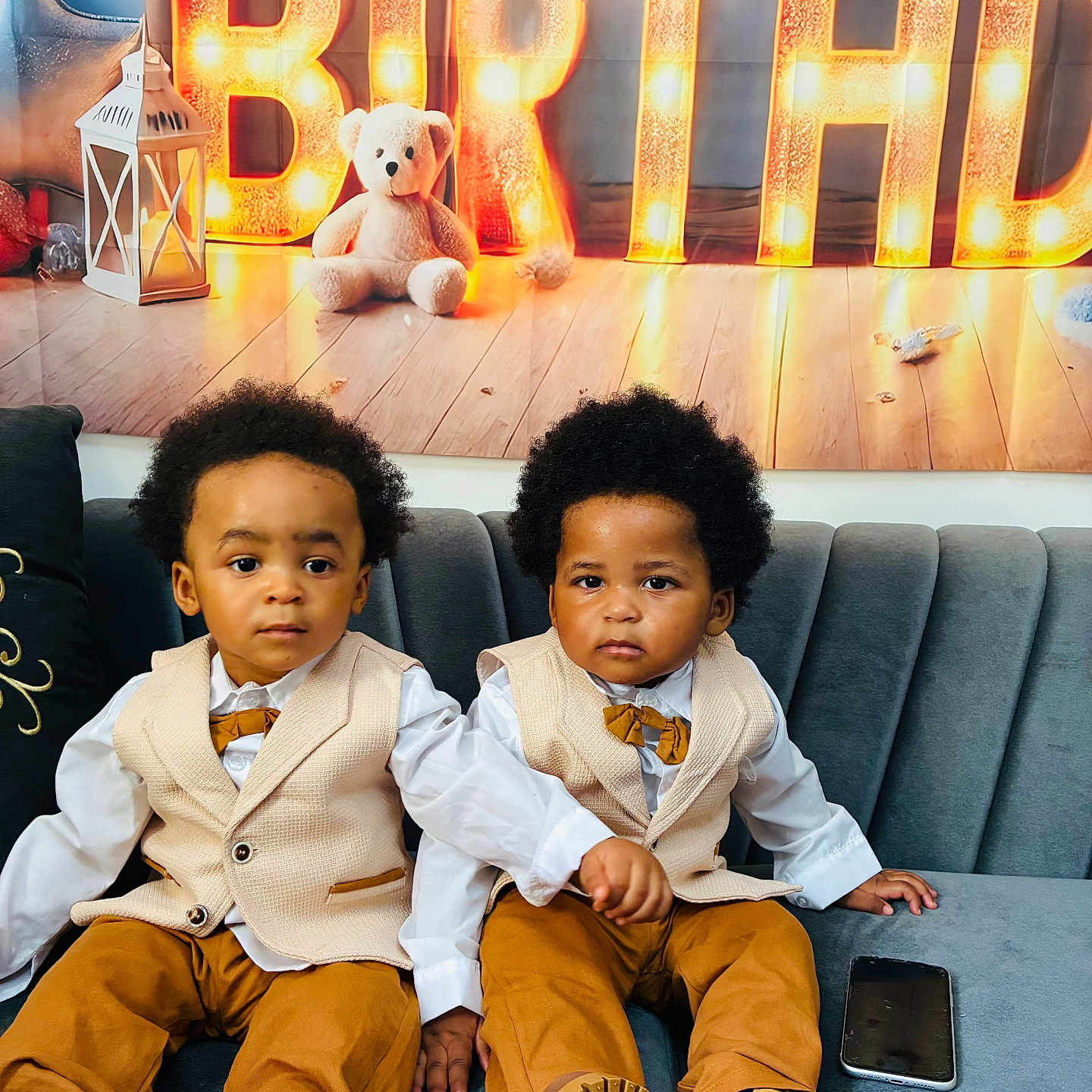 Soan Et Elyas a rejoint le concours — aidez-le/la à gagner de superbes lots ! bow_tie, brown_pants, child, couch, curly_hair, formal_wear, marquee_lights, neutral_expression, party_backdrop, plush_toy, portrait, sitting, smartphone, sofa, teddy_bear, toddler, twins, two_children, vests, wooden_floor