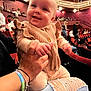 baby, child, person, hand, clothing, bracelet, theater, seat, audience, indoor, smile, happy, cute, jeans, ripped_jeans, red_seat, event, crowd, holding, portrait