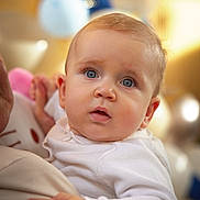 Stefan participe au concours pour gagner de l'argent avec cette photo : baby, balloons, blue_eyes, blurred_background, celebration, child, close_up, curious, cute, expression, face, hand, holding, indoor, infant, person, portrait, soft_skin, warm_light, white_clothing