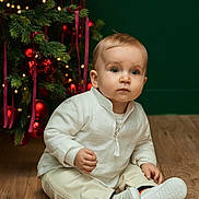 Stefan a rejoint le concours — aidez-le/la à gagner de superbes lots ! baby, child, infant, sitting, white_clothing, christmas_tree, ornaments, red_balls, holiday_decor, floor, wooden_floor, indoors, cute, curious, festive, lights, toddler, sock, shoe, portrait