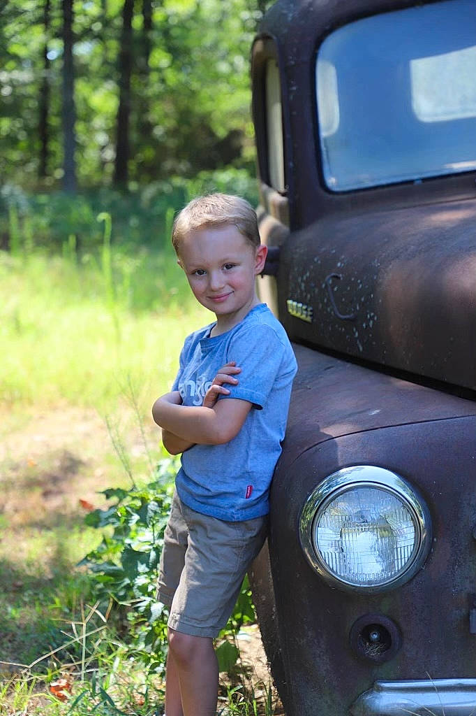Jaxton is registered to the contest to win money with this photo: automotive_design, automotive_exterior, automotive_lighting, automotive_tire, bumper, car, fender, grass, hood, joy, leaf, mode_of_transport, motor_vehicle, person, plant, shorts, smile, tree, vehicle, vehicle_door