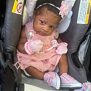 Leilani is registered to the contest to win money with this photo: baby, infant, car_seat, pink_dress, mittens, headband, flower, curly_hair, shoes, seatbelt, warning_label, blanket, indoor, cute, person, child, portrait, seated, closeup, soft_lighting