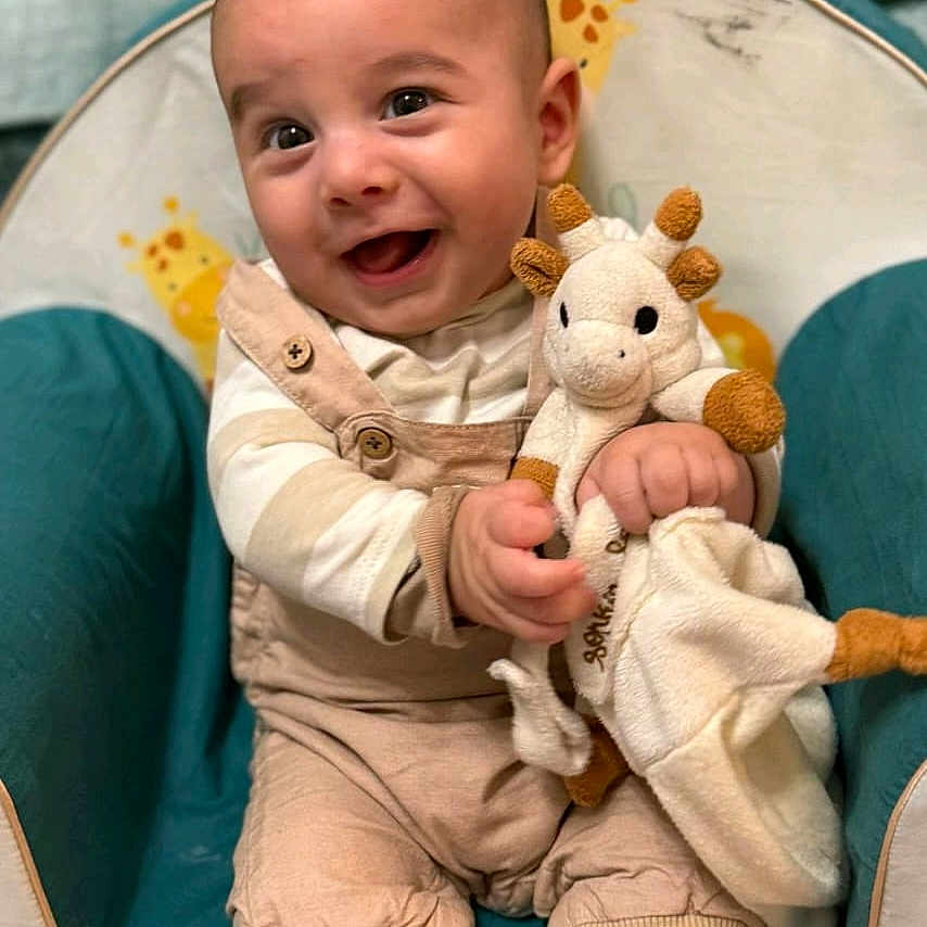 Arel participe au concours pour gagner de l'argent avec cette photo : baby, baby_chair, child, clothing, cute, feet, giraffe, hands, happy, home, indoors, infant, overalls, person, plush_toy, portrait, seated, smiling, striped_shirt, toy