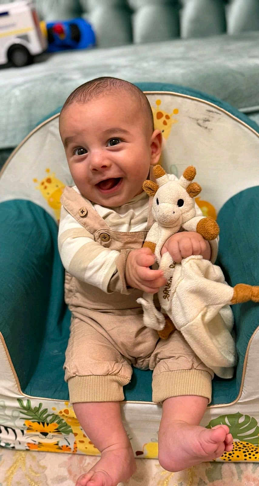 Arel participe au concours pour gagner de l'argent avec cette photo : baby, child, smiling, plush_toy, giraffe, baby_chair, happy, cute, indoors, clothing, overalls, striped_shirt, feet, hands, infant, portrait, toy, seated, person, home