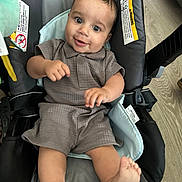 Enzio is registered to the contest to win money with this photo: baby, infant, child, smile, happy, face, eyes, feet, clothing, baby_carrier, seat, indoors, wooden_floor, fabric, cute, portrait, skin, hand, playful, relaxation