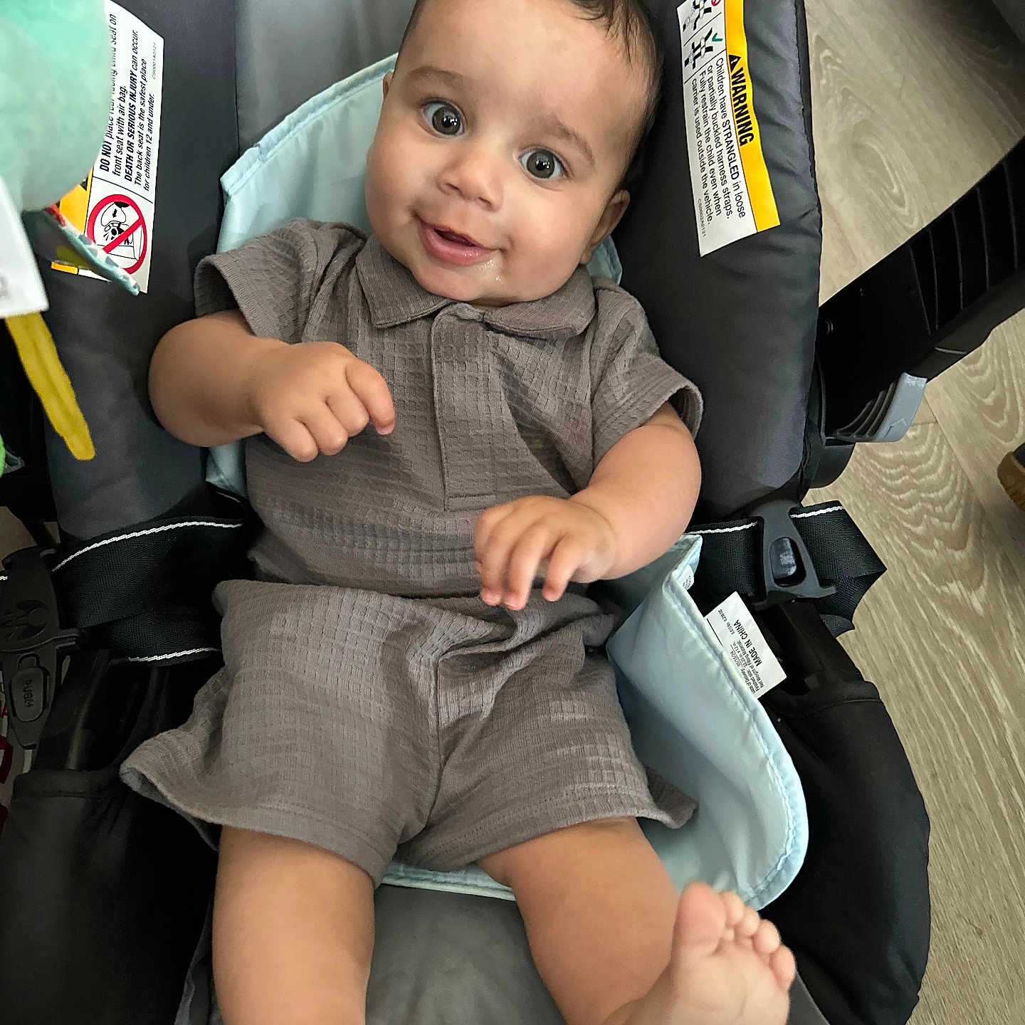 Enzio is registered to the contest to win money with this photo: baby, infant, child, smile, happy, face, eyes, feet, clothing, baby_carrier, seat, indoors, wooden_floor, fabric, cute, portrait, skin, hand, playful, relaxation