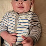 baby, infant, onesie, striped_clothing, hands, face, cheeks, cushion, soft_furniture, indoor, portrait, child, cute, smile, curious, seated, young_child, person, skin, head