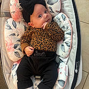 Alana is registered to the contest to win money with this photo: baby, infant, child, black_bow, leopard_print, pants, socks, baby_seat, floral_pattern, cushion, indoor, floor_tiles, cute, portrait, person, young_child, comfort, resting, clothing, headwear