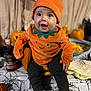 baby, child, pumpkin_costume, halloween, tablecloth, spiderweb_pattern, pumpkins, orange, black_pants, socks, happy, indoor, celebration, holiday, cute, festive, face, smile, costume, seasonal