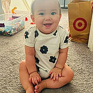 Naomi joined the competition — help win amazing prizes! baby, child, smiling, sitting, carpet, onesie, black_flower_pattern, hair_tuft, toy_bin, toys, shopping_bag, target_logo, indoor, home, floor, cute, happy, infant, person, portrait