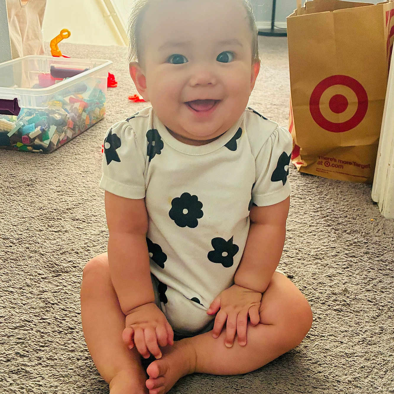 Naomi joined the competition — help win amazing prizes! baby, child, smiling, sitting, carpet, onesie, black_flower_pattern, hair_tuft, toy_bin, toys, shopping_bag, target_logo, indoor, home, floor, cute, happy, infant, person, portrait