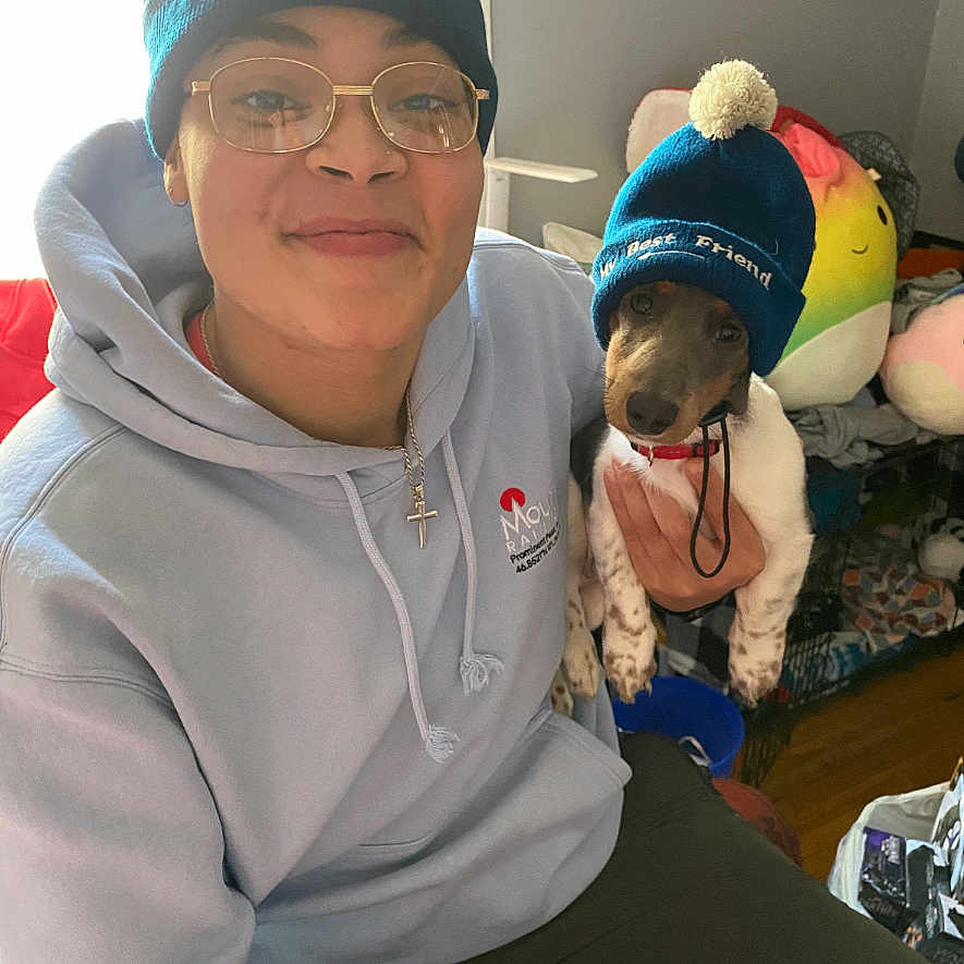 Cow Johnson joined the competition — help win amazing prizes! person, dog, beanie, glasses, hoodie, indoor, plush_toys, smiling, pet, seated, cross_necklace, blue_color, casual_clothing, small_dog, warm_lighting, cute, matching_outfits, pom_pom, friendship, home_interior