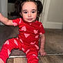toddler, child, pajamas, red_clothing, hearts_pattern, sitting, floor, wooden_floor, carpet, indoors, portrait, face, hair, pigtails, cute, young_child, eyes, smile, hand, person