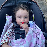 Elena joined the competition — help win amazing prizes! toddler, child, car_seat, blanket, lollipop, outdoor, curly_hair, face, hand, clothing, safety_harness, expression, pavement, grass, baby, person, cute, wrapped, warm, seat