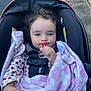 toddler, child, car_seat, blanket, lollipop, outdoor, curly_hair, face, hand, clothing, safety_harness, expression, pavement, grass, baby, person, cute, wrapped, warm, seat