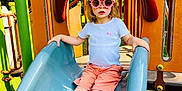 Chloé a rejoint le concours — aidez-le/la à gagner de superbes lots ! child, slide, playground, sunglasses, cap, shorts, tshirt, shoes, outdoor, summer, fun, play, park, toy, equipment, greenery, daylight, person, fashion, leisure