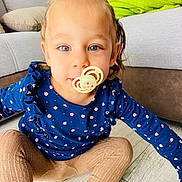 Chloé a rejoint le concours — aidez-le/la à gagner de superbes lots ! toddler, child, pacifier, blue_eyes, blue_top, floral_pattern, beige_tights, sitting, wooden_floor, living_room, couch, blanket, indoor, cute, portrait, young_child, smiling, person, home, cozy