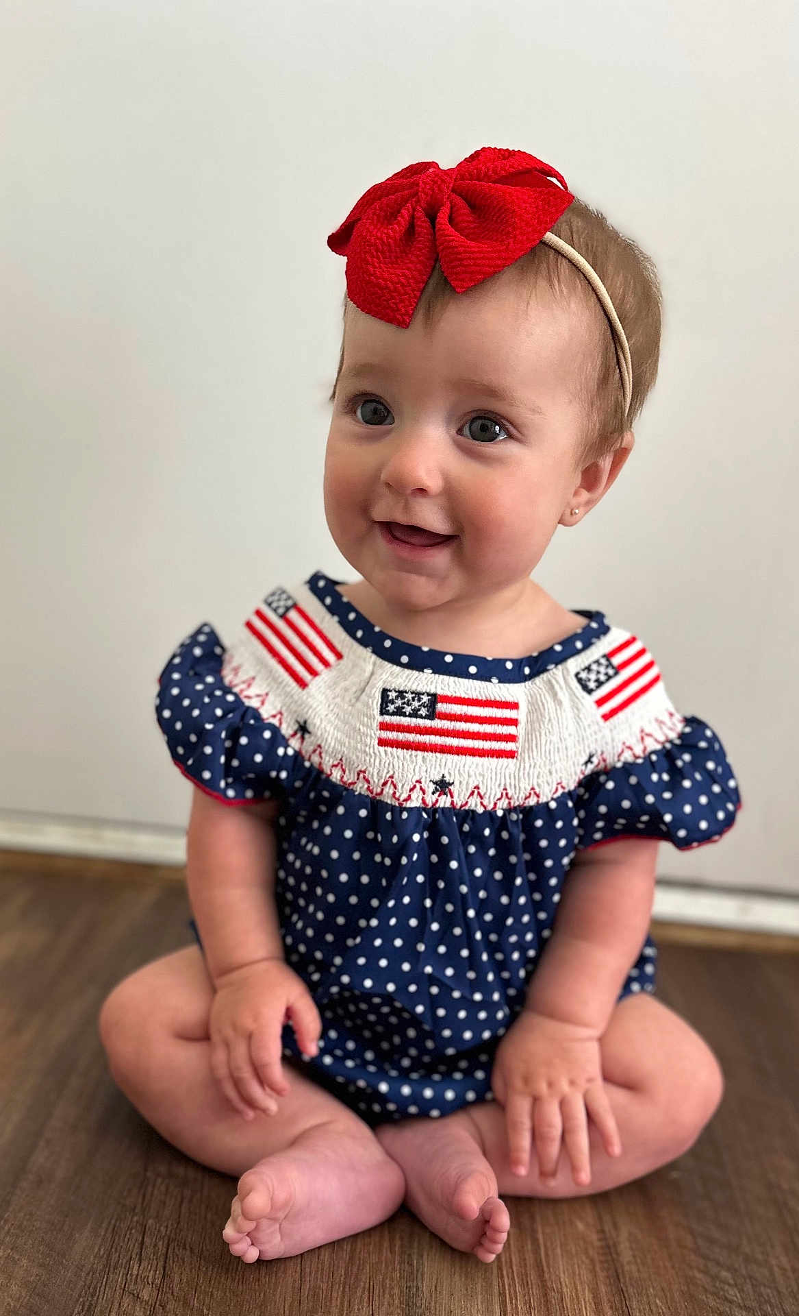 Emberlynn joined the competition — help win amazing prizes! baby, child, cute, dress, face, feet, floor, girl, hands, happy, headband, indoor, infant, polka_dot, portrait, red_bow, sitting, skin, smile, wooden_floor