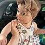 baby, child, headband, bow, floral_dress, infant, hand, car_interior, cushion, pattern, cute, portrait, person, young_child, face, skin, clothing, holding, indoor, closeup