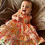 baby, child, smiling, dress, floral_pattern, blanket, happy, cute, infant, person, clothing, fabric, portrait, lying_down, indoors, skin, head, hand, earrings, colorful