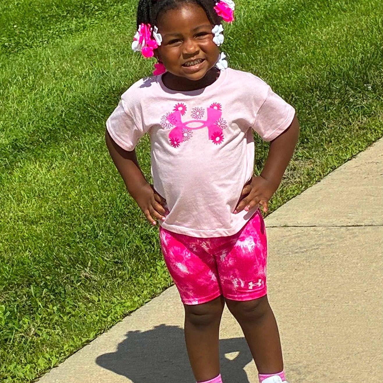 Navaya joined the competition — help win amazing prizes! child, girl, smile, outdoor, sidewalk, grass, sunlight, pink_clothing, shorts, tshirt, sneakers, hair_accessories, happy, standing, casual, daytime, cute, confident, person, portrait