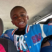 Noa is registered to the contest to win money with this photo: child, boy, smiling, portrait, selfie, car, vehicle, passenger, backseat, indoors, jacket, blue_clothing, varsity_jacket, t_shirt, short_hair, teeth, happy, sitting, automobile, daylight