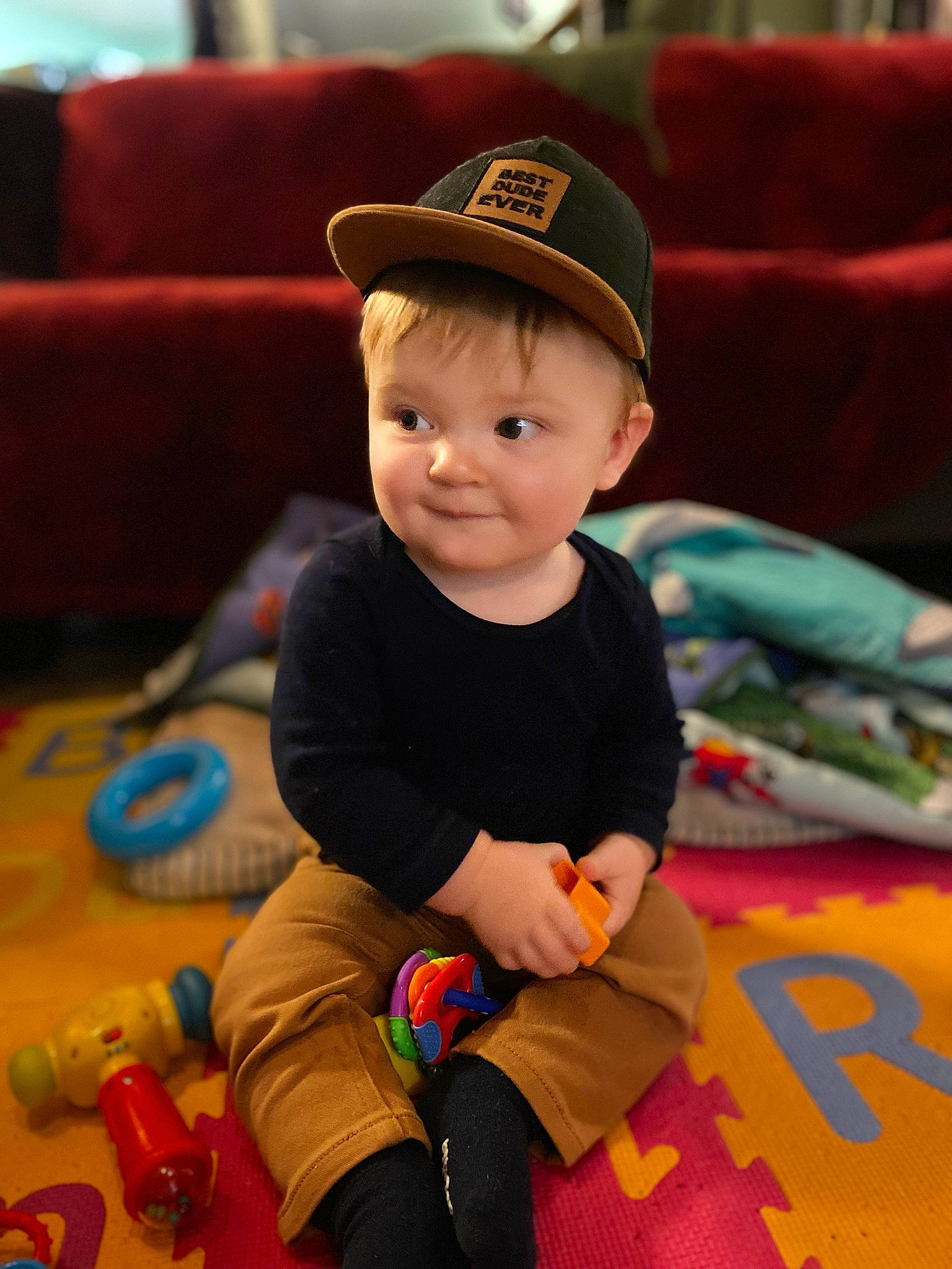 Greyson is registered to the contest to win money with this photo: baby, baby_playing_with_toys, baby_toddler_clothing, baseball_cap, cap, cheek, child, flooring, fun, happy, hat, leg, leisure, person, photograph, room, sitting, skin, smile, toddler