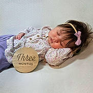 Scotlynne May is registered to the contest to win money with this photo: baby, infant, sleeping, headband, bow, floral_clothing, wooden_plaque, three_months, soft_texture, white_background, peaceful, cute, portrait, newborn, child, lying_down, close_up, indoors, young_baby, resting
