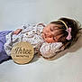 baby, infant, sleeping, headband, bow, floral_clothing, wooden_plaque, three_months, soft_texture, white_background, peaceful, cute, portrait, newborn, child, lying_down, close_up, indoors, young_baby, resting