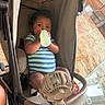 Dalton is registered to the contest to win money with this photo: baby, bottle, stroller, infant, child, fan, onesie, striped_clothing, indoor, carpet, glass_table, footwear, relaxing, comfort, baby_fan, cute, seated, hand, face, person