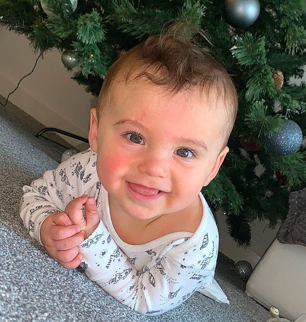 Lewis is registered to the contest to win money with this photo: baby, baby_toddler_clothing, cheek, christmas_tree, eye, face, facial_expression, gesture, green, hairstyle, happy, head, holiday_ornament, human_body, joy, nose, person, sleeve, smile, standing