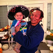 Ryker joined the competition — help win amazing prizes! baby, child, adult, man, sombrero, poncho, smile, happy, holding, outdoor, pumpkins, fall_decorations, window, door, person, clothing, festival, celebration, family, portrait