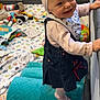 baby, baby_girl, blanket, cheerful, child, clothing, colorful, cushion, cute, denim_dress, happy, headband, indoor, play_area, playpen, smiling, soft_texture, standing, toddler, toys