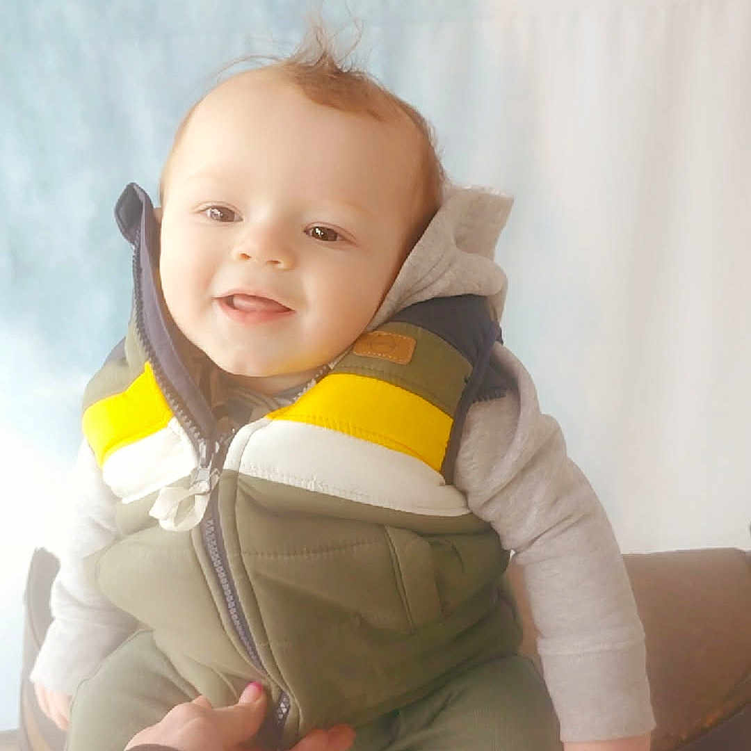 Liam joined the competition — help win amazing prizes! baby, child, smile, hoodie, vest, hand, support, indoor, soft_light, weekend, text_overlay, happy, cute, portrait, casual_clothing, infant, seated, person, face, warm