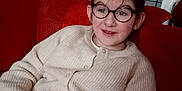 Aureline a rejoint le concours — aidez-le/la à gagner de superbes lots ! child, girl, glasses, sweater, red_couch, stuffed_animal, plush_toy, indoor, smiling, seated, cabinet, cozy, home, casual, portrait, relaxed, person, furniture, happy, comfortable