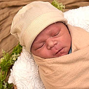 Isaiah joined the competition — help win amazing prizes! baby, newborn, infant, swaddled, beanie_hat, hat, sleeping, closed_eyes, face, cheeks, nose, blanket, soft_texture, beige, cozy, portrait, newborn_photography, basket, greenery, peaceful
