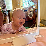 Summer is registered to the contest to win money with this photo: baby, mirror, reflection, smile, face, onesie, pink, patterned_clothing, infant, happy, indoor, bed, blanket, toy, home, window, light, furniture, curtains, playtime