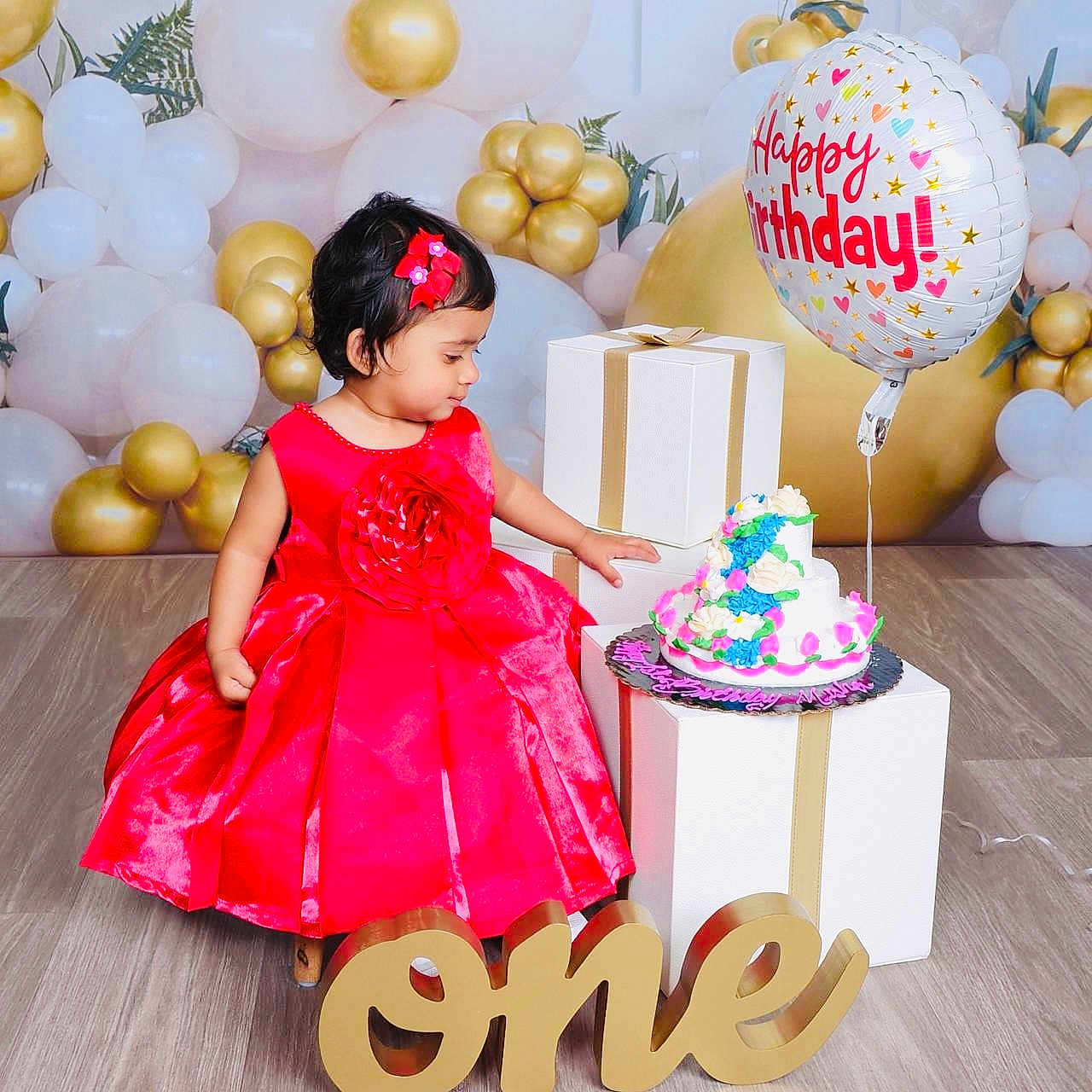 Misha is registered to the contest to win money with this photo: balloons, birthday, cake, celebration, child, colorful, decorations, festive, floor, flower_hairclip, gift_boxes, happy_birthday, holiday, indoor, one_year, party, person, red_dress, smiling, toddler