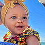 baby, blue_sky, bow, cheerful, child, closeup, colorful_clothing, cute, daylight, family, happy, headband, holding, infant, ocean, outdoor, patterned_dress, person, portrait, smiling
