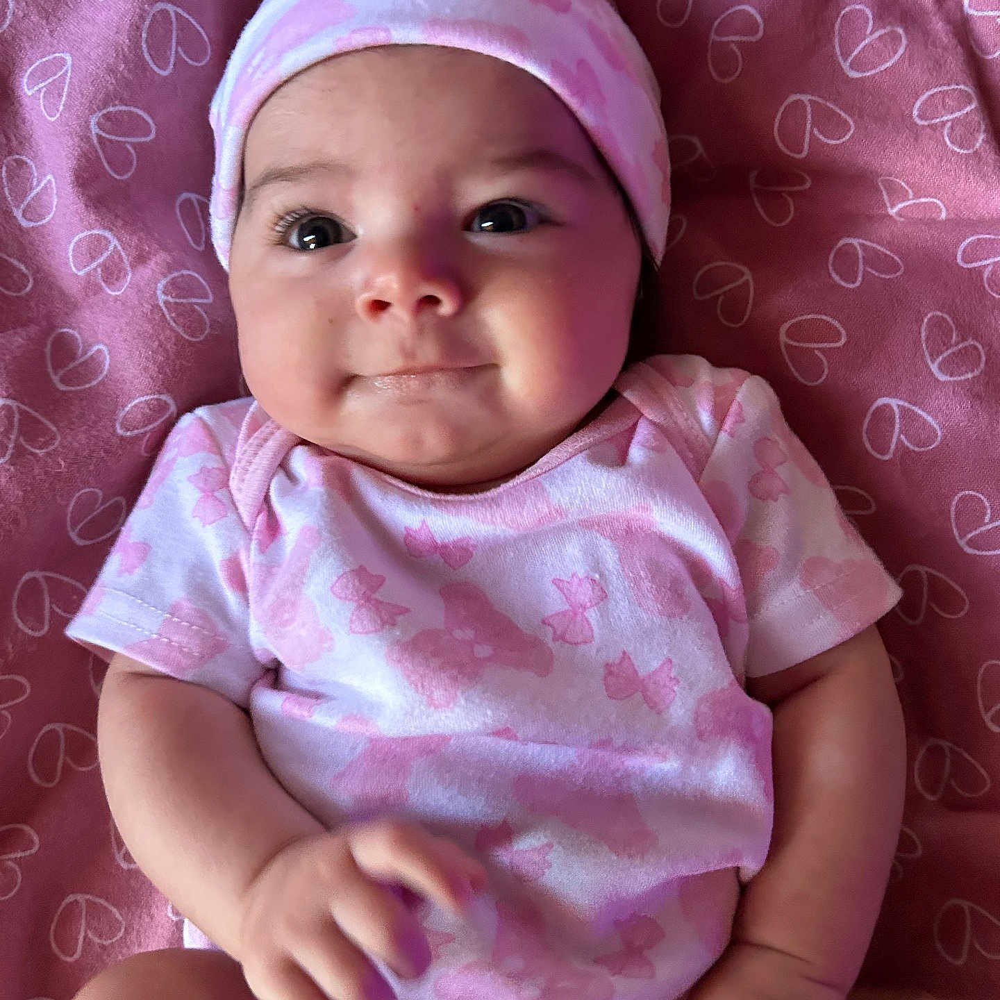 Sarajean is registered to the contest to win money with this photo: adorable, baby, blanket, child, closeup, cute, face, hand, hat, heart_pattern, indoors, infant, lying_down, onesie, person, pink, portrait, skin, smiling, young