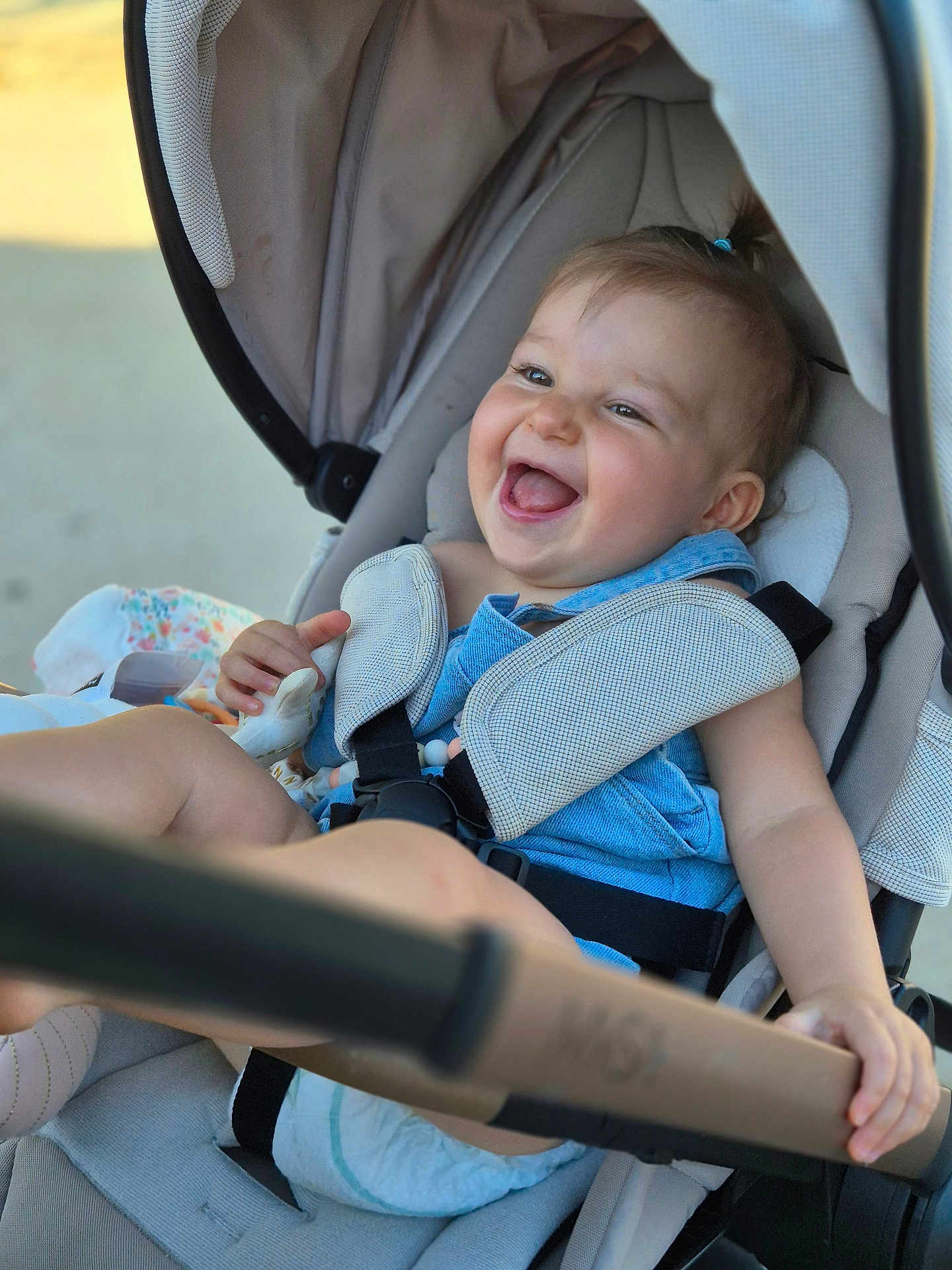 Swanne participe au concours pour gagner de l'argent avec cette photo : baby, child, stroller, smiling, happy, blue_clothing, seatbelt, infant, cute, portrait, outdoor, sunlight, baby_harness, diaper, hand, face, person, young_child, joyful, candid