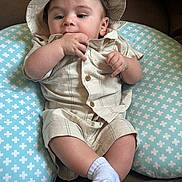 Trystan is registered to the contest to win money with this photo: baby, baby_garment, beige_outfit, chewing, child, clothing, couch, cushion, cute, face, hand, hat, indoor, infant, portrait, relaxed, seated, socks, soft_furniture, young_child