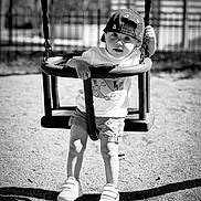 Ezio a rejoint le concours — aidez-le/la à gagner de superbes lots ! black_and_white, cap, casual_clothing, child, curious, fence, fun, hat, outdoor, person, play, playground, recreation, shadow, shorts, sneakers, sunlight, swing, toddler, young