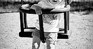 Ezio participe au concours pour gagner de l'argent avec cette photo : baby_swing, black_and_white, cap, casual_clothing, chain, child, fence, fun, hat, outdoor, person, play, playground, shadow, shorts, sneakers, summer, sunlight, swing, toddler