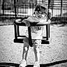 baby_swing, black_and_white, cap, casual_clothing, chain, child, fence, fun, hat, outdoor, person, play, playground, shadow, shorts, sneakers, summer, sunlight, swing, toddler