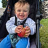 baby, child, toddler, smiling, portrait, stroller, apple, fruit, outdoor, grass, park, sunlight, harness, seated, clothing, blue_pants, white_shirt, happy, face, photography