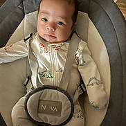 Grimm is registered to the contest to win money with this photo: baby, baby_accessory, bouncer_seat, child, close_up, cozy, cushion, dinosaur_print, eyes, fabric, face, harness, indoor, infant, legs, onesie, portrait, sleepwear, soft_lighting, wood_floor