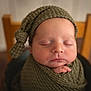 newborn, baby, sleeping, knitted_hat, blanket, infant, peaceful, portrait, closeup, soft_focus, wooden_chair, wrapped, child, indoors, cute, skin, hand, peace, rest, warm_tones